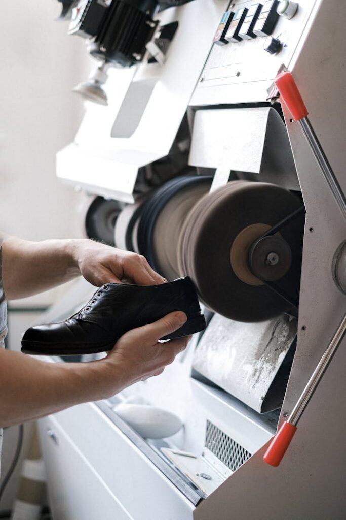 szewc-miasteczko-śląskie Zbliżenie na rzemieślnika polerującego skórzany but za pomocą maszyny przemysłowej wewnątrz warsztatu.